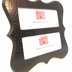 May include: A black, double-aperture license frame with a textured, faux-leather finish. The frame has a decorative, curved shape and includes the text "Barber & Cosmetology License Frame" and the logo "Familiar Faces".