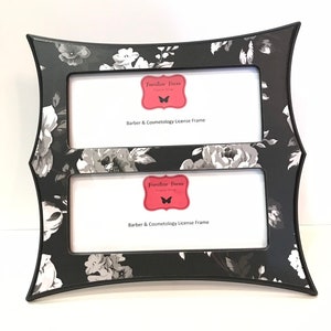 May include: A double picture frame with a black and white floral design. The frame has a curved shape and features a repeating pattern of grey and white flowers on a black background. The frame includes the text "Familiar Faces Frame Shop" and "Barber & Cosmetology License Frame".