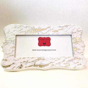 May include: A rectangular license frame with a white marble design and gold accents. The frame has a decorative, scalloped edge and features the text "Barber & Cosmetology License Frame".