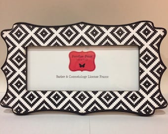 May include: A black and white patterned license frame with a rectangular opening. The frame has a decorative, scalloped edge and features a repeating diamond pattern. The text "Barber & Cosmetology License Frame" is visible.