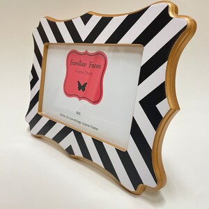 May include: A decorative picture frame with a black and white chevron pattern. The frame has a gold-coloured trim and a rectangular opening for a 20x13 cm photo. The frame includes the text "Familiar Faces Frame Shop" and "Barber & Cosmetology License Frame".