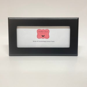 May include: A black rectangular frame with a white interior. The frame features the text "Familiar Faces" and "Barber & Cosmetology License Frame". It is designed to display a professional license.