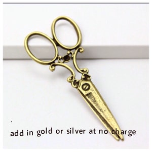 May include: Ornate, antique-style scissors in a gold tone. The scissors have a decorative design on the handles and blades. The text "add in gold or silver at no charge" is at the bottom of the image.
