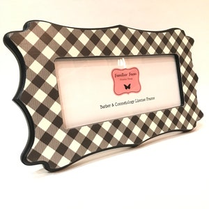 May include: A license frame with a brown and cream gingham pattern. The frame has a black border and a rectangular aperture. The text "Barber & Cosmetology License Frame" is visible on a pink tag.