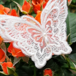May include: A white lace butterfly with a pearl accent, resting on a bed of orange rosebuds.