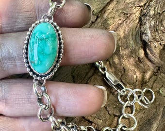 May include: A silver chain bracelet featuring a central oval turquoise stone set in a beaded bezel. The bracelet is constructed with round interlocking silver links and includes a lobster claw clasp with an adjustable extension chain at the end.