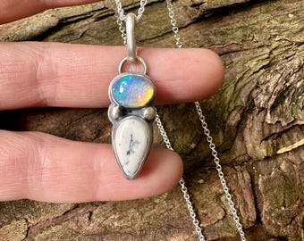 May include: A silver pendant necklace featuring a teardrop-shaped white dendritic opal with black fern-like inclusions and a smaller oval-shaped iridescent opal set above it. The stones are encased in a brushed silver setting on a thin silver chain.