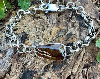May include: A silver bracelet with a rectangular, brown and green stone centerpiece. The bracelet features a chain link design with a clasp closure. The stone has a unique pattern and is set in a silver bezel.