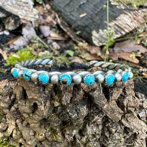 May include: A silver bracelet with a twisted design and turquoise stones.