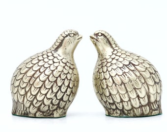 May include: Two silver metal bird figurines facing each other. The birds have detailed feather patterns and are in a romantic pose.
