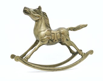 May include: A gold-colored metal rocking horse figurine. The horse is in a galloping pose with its head turned to the side. The rocking base is made of metal and has a simple design.
