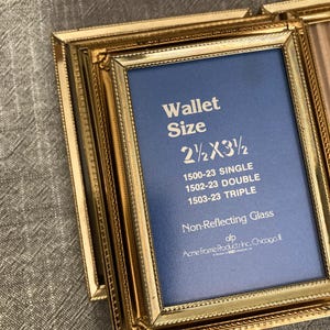 May include: A gold-colored picture frame with a blue mat and the text "Wallet Size 2 1/2 X 3 1/2" and "Non-Reflecting Glass". The frame has a decorative border and the text "ofp Acme Frame Products Inc. Chicago, IL" is printed on the mat.