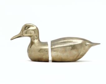May include: A brass duck-shaped bookend set, split in half to hold books. The duck has a detailed head and a smooth body. The metallic finish gives it a vintage look. The bookends are designed to be functional and decorative.