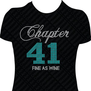Puede incluir: Camiseta negra con un diseño de pedrería blanca que dice "Chapter 41 Fine as Wine". El número 41 está en pedrería turquesa.