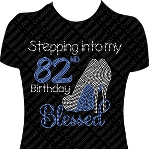 May include: A black t-shirt with a blue and white rhinestone design that says "Stepping into my 82nd Birthday Blessed".