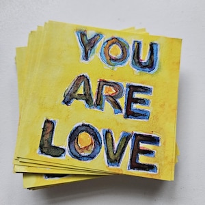 May include: A stack of yellow cards with the words "YOU ARE LOVE" written in black and blue paint.