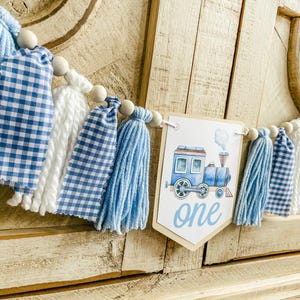 May include: Blue and white tassel garland with a wooden bead and a blue train with the word "one" on a white banner.