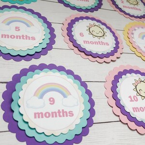 Puede incluir: Un conjunto de diez tarjetas de hitos para beb&eacute;s coloridas con dise&ntilde;os de arco&iacute;ris y sol. Cada tarjeta presenta un n&uacute;mero del 1 al 10 y la palabra "meses".