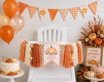 May include: A high chair banner featuring a central sign with a pumpkin illustration and the text one, flanked by orange and cream yarn tassels and wooden beads. The scene includes orange balloons, a pennant banner, and a cake with pumpkin decor.