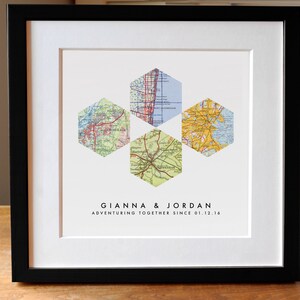May include: A framed wall art piece featuring four hexagonal map cutouts arranged in a cross pattern on a white background. Below the maps, the text reads GIANNA & JORDAN ADVENTURING TOGETHER SINCE 01.12.16 in black, sans-serif capital letters.