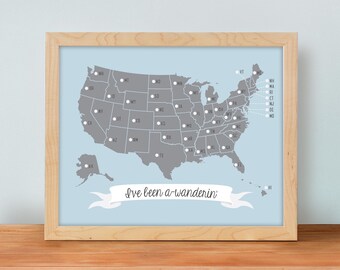 May include: A framed map of the United States in gray on a light blue background, featuring white state abbreviation dots and a white banner at the bottom with the black cursive text I've been a-wanderin' inside a light wood frame.