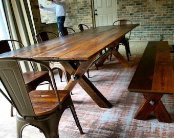 May include: A rustic wooden dining table with a metal cross-shaped base and a matching bench. The table is surrounded by metal chairs with wooden seats. The table and bench are both made of reclaimed wood.