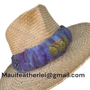 May include: A wide-brimmed straw hat with a purple and green feather trim. The hat is made of woven straw and has a slightly rounded crown. The feather trim is made of natural feathers and is attached to the hat with a band.