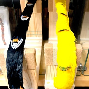 Puede incluir: Dos boas de plumas, una negra con detalles blancos y otra amarilla con detalles verdes, expuestas en soportes de madera.