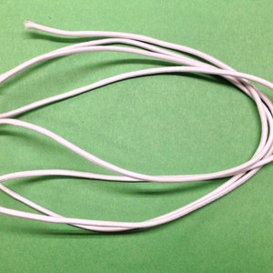 May include: A white elastic cord, approximately 12 inches long, is coiled on a green surface.