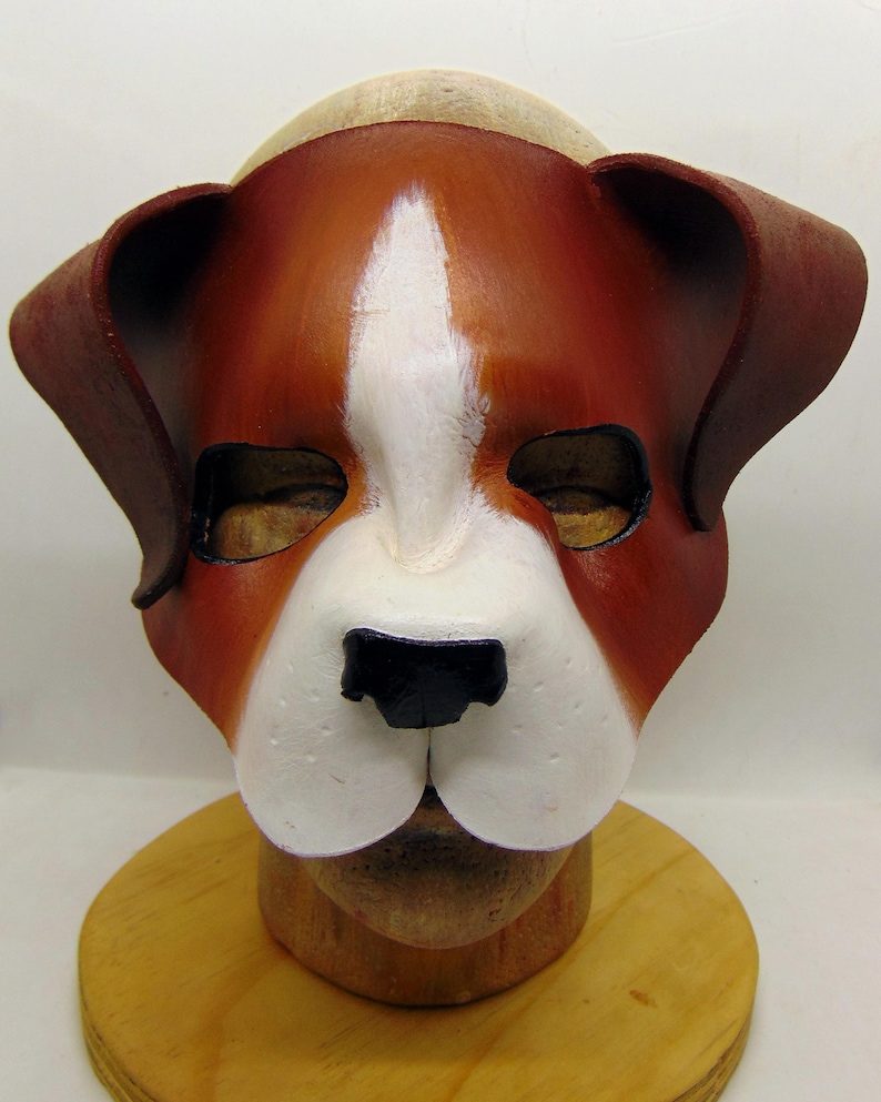 May include: A brown and white leather dog mask with black nose and white fur details. The mask is on a wooden mannequin head.