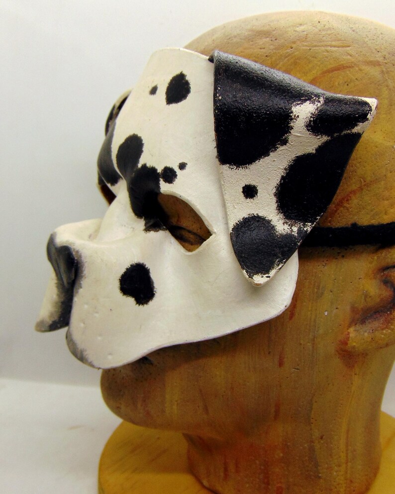 May include: A white and black dalmatian dog mask with black spots. The mask has a cutout for the eyes and a nose.