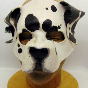May include: A white and black dalmatian dog mask with black ears and a black nose. The mask is made of leather and has a realistic look.