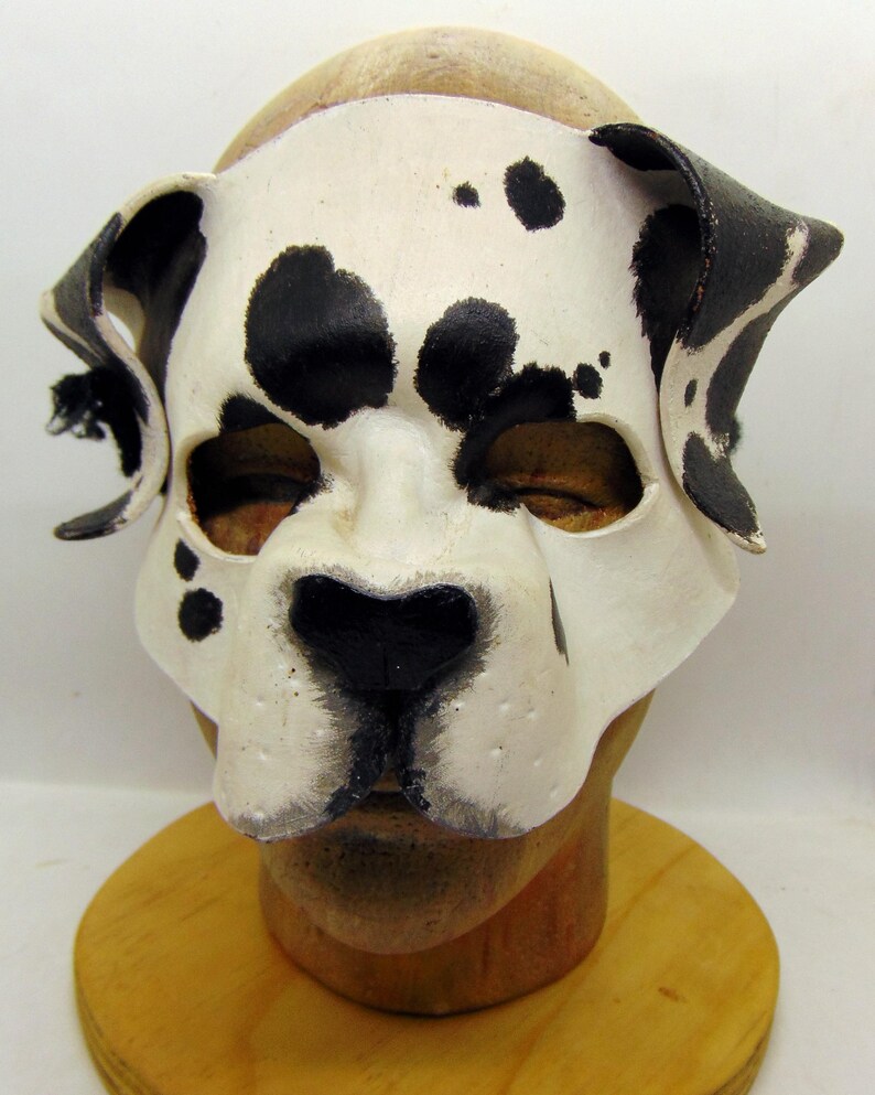 May include: A white and black dalmatian dog mask with black ears and a black nose. The mask is made of leather and has a realistic look.