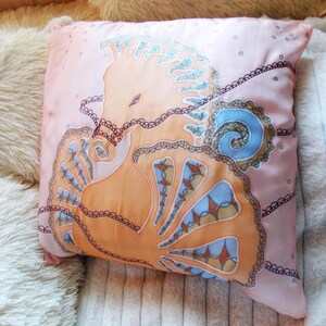 May include: A pink silk pillow with a hand-painted design of a seahorse with intricate details in shades of orange, blue, and brown.