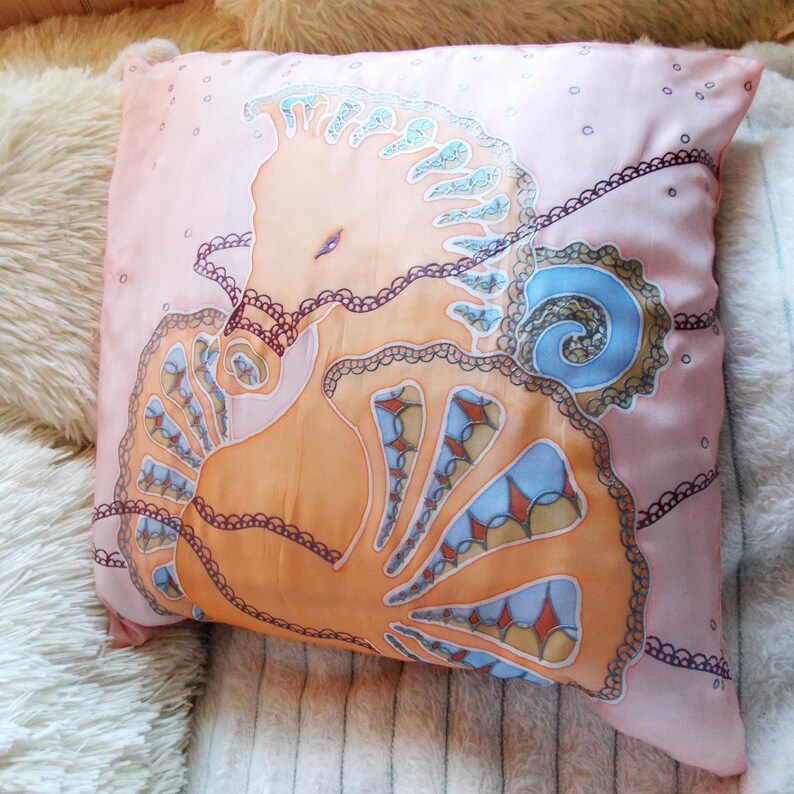 May include: A pink silk pillow with a hand-painted design of a seahorse with intricate details in shades of orange, blue, and brown.