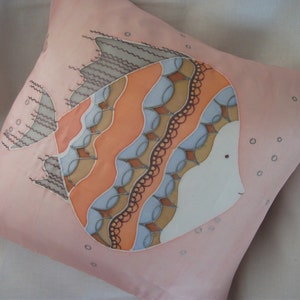 Puede incluir: Una almohada rosa con un dise&ntilde;o pintado a mano de un pez estilizado con detalles en naranja, marr&oacute;n y azul. El pez est&aacute; rodeado de peque&ntilde;os c&iacute;rculos.