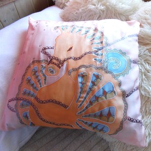 May include: A pink pillow with a hand-painted design of an orange seahorse with blue and brown accents. The seahorse is surrounded by a black lace pattern.