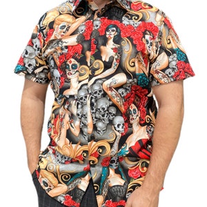 May include: A short-sleeved button-down shirt with a black background and a colorful print of skulls, roses, and women with sugar skull makeup.