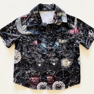 May include: A black short-sleeved button-down shirt with a celestial print featuring planets, stars, and constellations. The shirt has a classic collar and a pocket on the left chest.