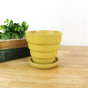 May include: A yellow ceramic planter with a saucer. The planter has a fluted design and is made in a vintage style.