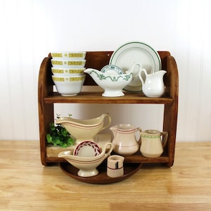 May include: A wooden shelf displays a collection of vintage dishware. The items include bowls with yellow and green designs, gravy boats with red stripes, small pitchers, and a plate with a green border. The shelf is made of dark wood.