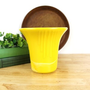 May include: A bright yellow ceramic vase with a fluted design. The vase is sitting on a wooden surface.