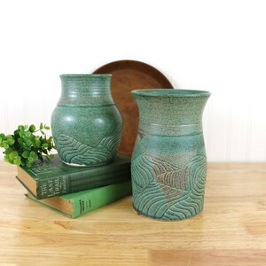 May include: Two green ceramic vases with a textured, wavy design. The vases are sitting on a stack of books.