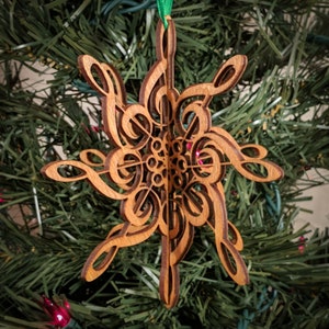 May include: A wooden Christmas ornament shaped like a snowflake with intricate details. The ornament is made of laser-cut wood and features a design of musical notes.