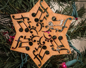 Op de afbeelding: Een houten stervormige kerstversiering met een uitgesneden ontwerp van muzieknoten en sleutels. De versiering is bruin en heeft een groen lint aan de bovenkant.