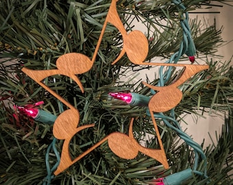 Op de afbeelding: Een houten stervormige kerstversiering met een ontwerp van muzieknoten. De ornament is bruin en hangt aan een groene kunstkerstboom.