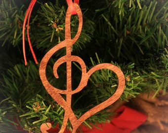 May include: A wooden Christmas ornament shaped like a treble clef with a heart cut out of the center. The ornament is hanging on a Christmas tree.