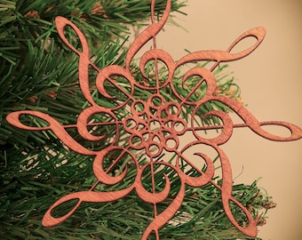 May include: A wooden Christmas ornament shaped like a snowflake, made from intricately cut musical notes. The ornament is brown and has a red ribbon attached to the top.