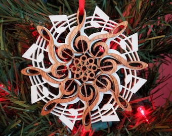 Pode incluir: Enfeite de Natal de madeira branca em forma de floco de neve com um design de madeira castanho de notas musicais e claves de sol.