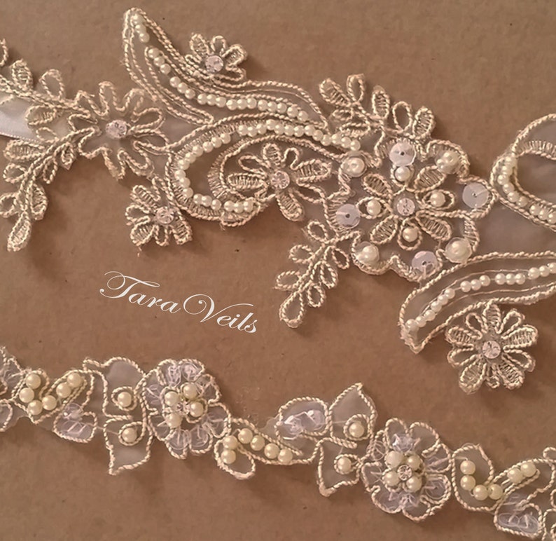 May include: Ivory lace trim with floral and leaf designs, embellished with pearls and sequins. The text "Tara Veils" is visible. This delicate trim is suitable for bridal wear and other special occasion projects.